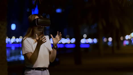 Eine-Junge-Frau-Mit-Virtual-Reality-Brille-Bewegt-In-Der-Nächtlichen-Stadt-Ihre-Hände-Und-Meistert-Die-Anwendungsoberfläche.-VR-Technologien-Der-Zukunft-Im-Alltag.-Virtual-Reality-Spiele
